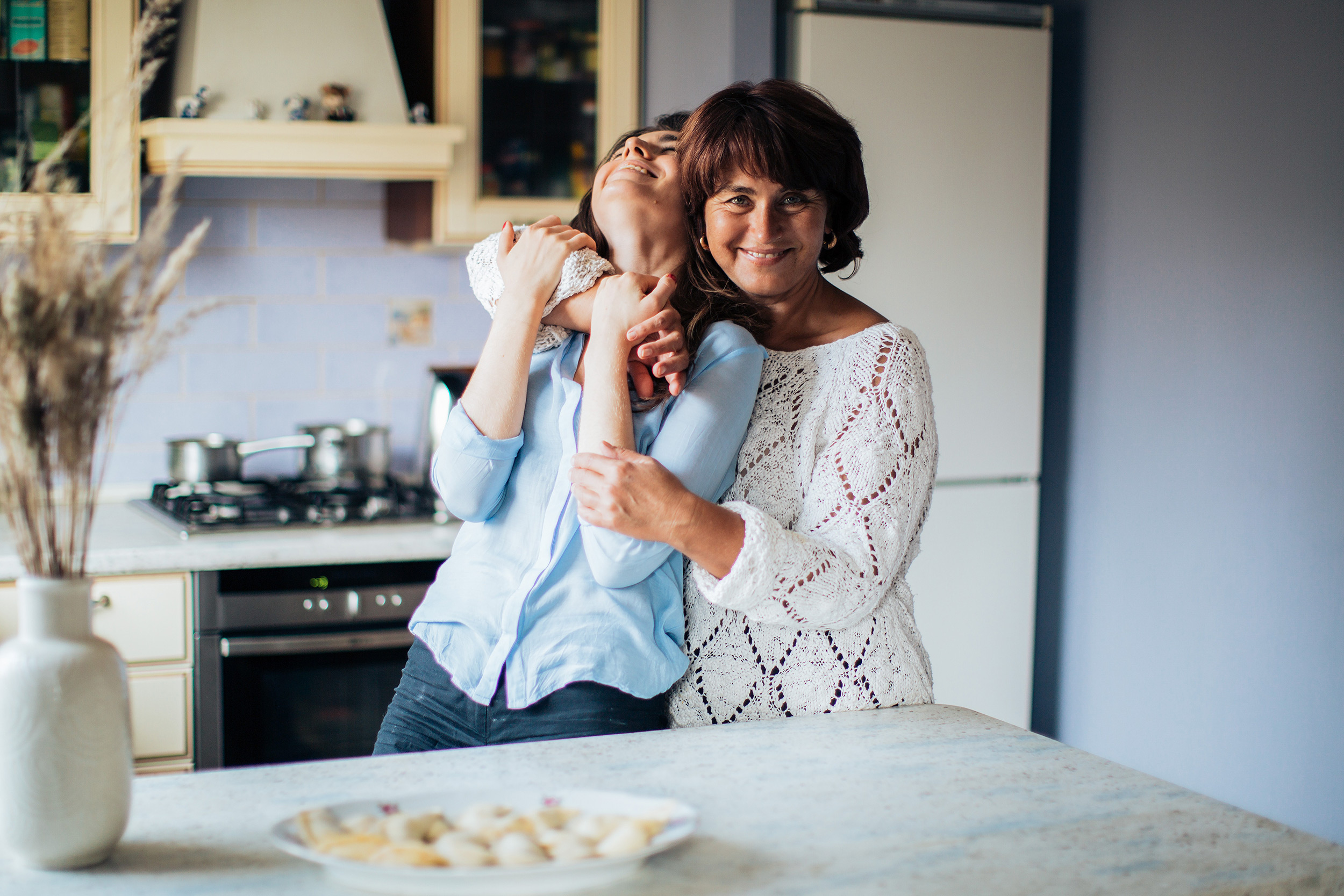a mother hugging her adult daughter in the kitchen